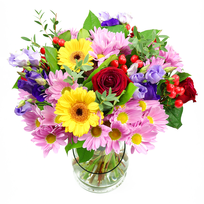 A tall, overflowing bouquet of mixed blooms is arranged in a cylindrical clear glass vase, photographed in front of a white background so that each colour and shape is easy to imagine. In the centre, velvety deep red roses spiral open, their rich petals layered closely, conveying a sense of classic romance and focal depth. Nestled among them, two radiant yellow gerbera daisies stretch their broad petals outward, circling dark brown-orange centres that resemble miniature suns and bring a warm, friendly brightness to the piece. Encircling this heart of the bouquet, a profusion of pink daisies or chrysanthemums adds generous volume; their many slender petals and tiny yellow centres create a soft, feathery texture that tempers the stronger reds and yellows. Intertwined with these are elegant purple and lavender lisianthus, their bell-shaped flowers and softly curved stems introducing cool, calming tones, much like the peaceful feel of nearby West Byfleet Recreation Ground on a quiet afternoon. Between petals, small clusters of shiny red hypericum berries peek through, their round, polished forms contributing playful contrast and a hint of seasonal festivity. A mixture of lush greenery weaves throughout-broad, dark leaves providing a sturdy frame, and lighter green, more slender sprigs adding height, movement, and a sense of garden freshness. Through the clear glass vase, straight, cleanly trimmed stems can be seen gathered in clear water, a detail that reflects the work of an attentive local florist such as Flower Delivery West Byfleet. Overall, the arrangement feels joyful yet refined, a versatile mixed bouquet suitable for birthdays, housewarmings, or simply brightening a hallway or dining table anywhere in West Byfleet and the surrounding lanes.